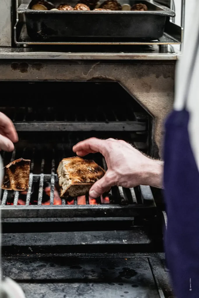 Chef saisissant une viande sur le grill Josper au charbon de bois à Narbonne.